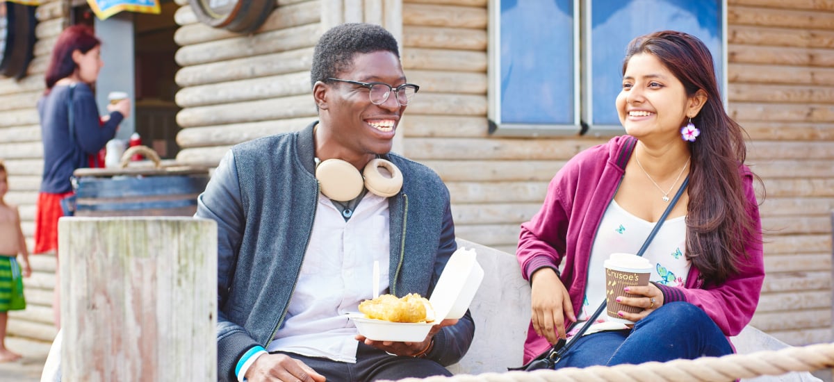 Two students enjoy fish and chips and coffee on the beach.